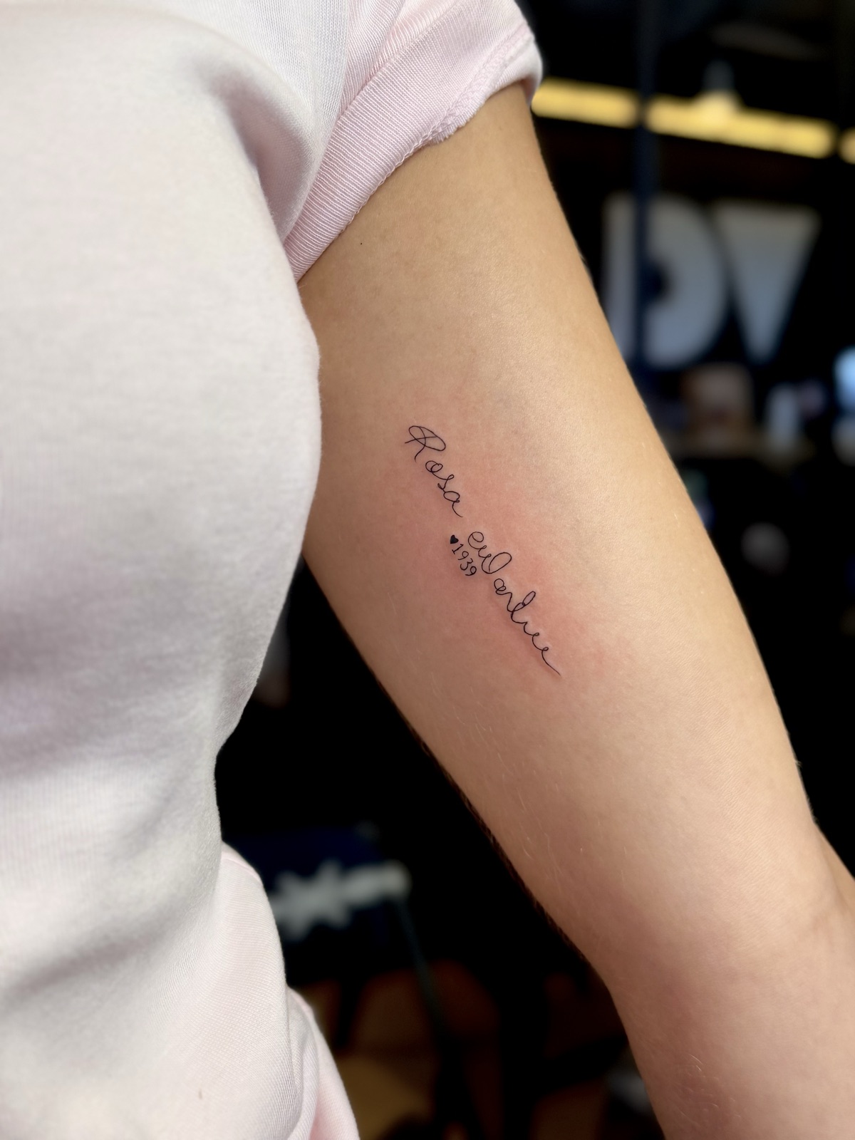 Nome "Rosa" em letra cursiva de traço fino com coração e o ano 1939, na parte interna do braço. Por Dudis (Maria Eduarda Freitas), na ADV Tattoo.
