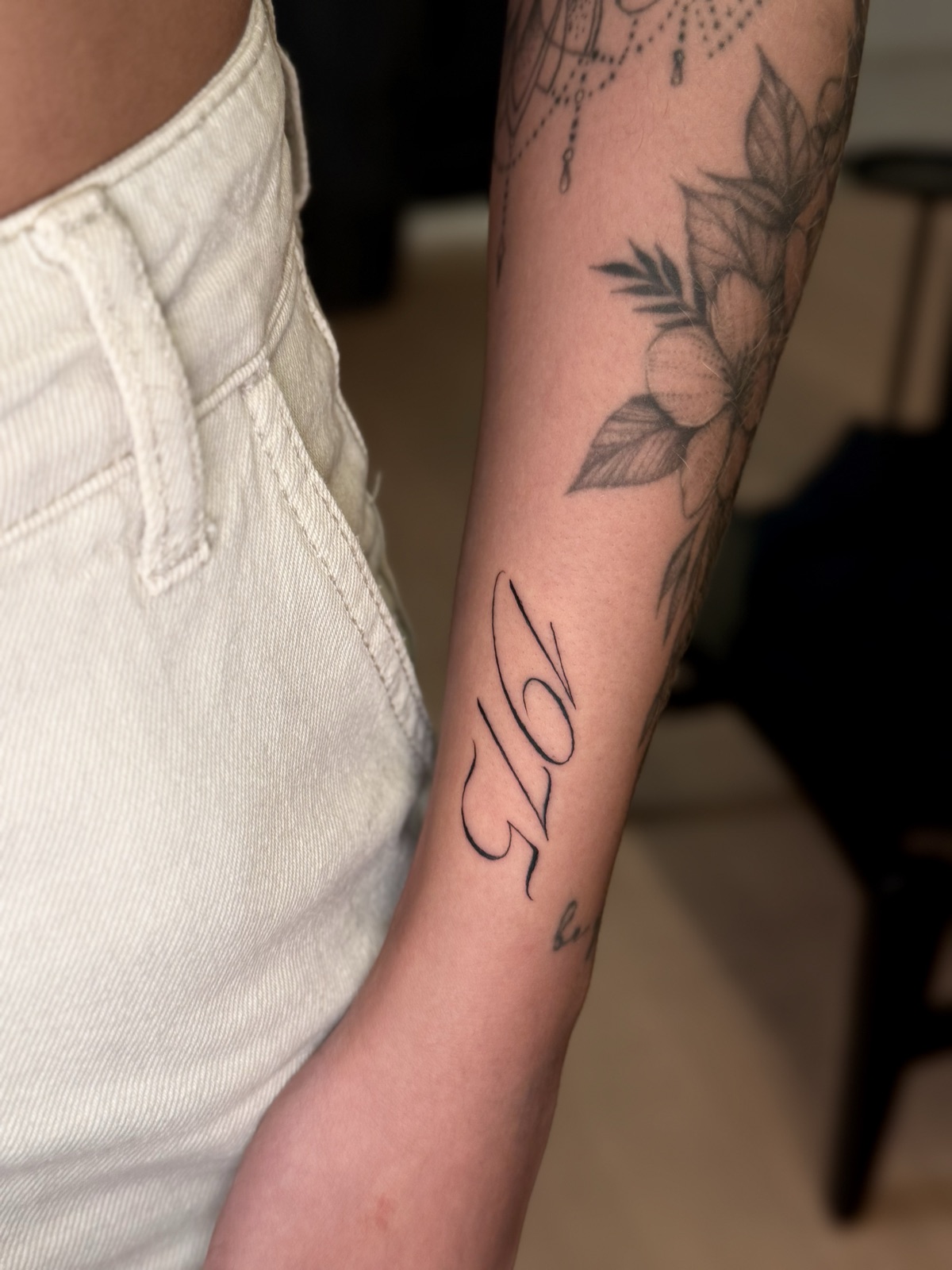 Número 1975 em lettering caligráfico de traço contrastado, no antebraço. Por Dudis (Maria Eduarda Freitas), na ADV Tattoo.