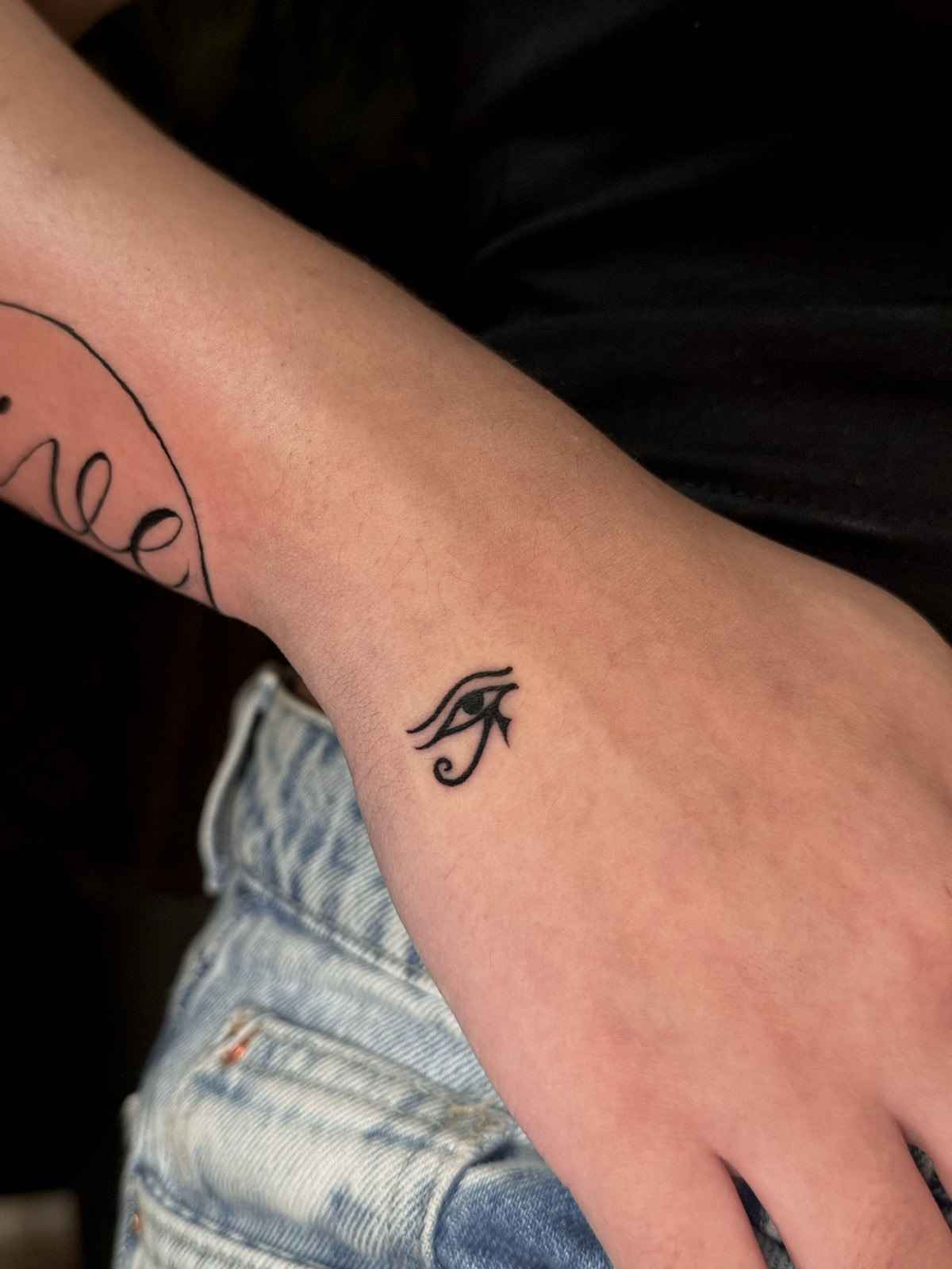 Olho de Hórus em traço preto sólido, pequeno, na lateral da mão. Por Dudis (Maria Eduarda Freitas), na ADV Tattoo.